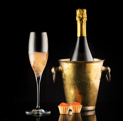 Red caviar and champagne in a bottle and a glass on a black background