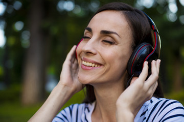 Close up funny portrait of young pretty hipster girl listening music on big earphones, posing at city center at sunny summer,smiling,teen,cool accessories,laugh