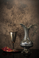 Retro still life with jug wine, metal goblet and a pomegranate
