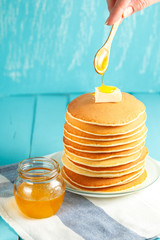 Woman pouring honey onto stack of pancakes with butter on top