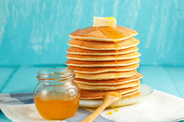Stack of pancake with honey and butter on light-blue background