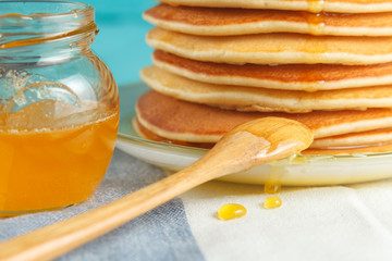 Close up of stack of pancake with pouring honey, wooden spoon and jar of honey