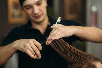 The hands of young barber making haircut to attractive bearded man in barbershop