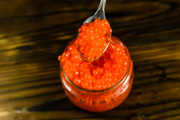 Red caviar in a spoon above the glass jar