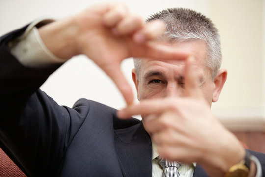 Mature businessman looking through square frame making by fingers