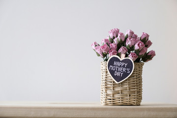 Happy mothers day message on wood heart and pink paper roses in basket on the table with copy space minimal style © ArtBackground