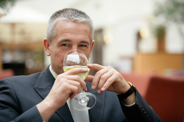 Gray-haired senior businessman drinking wine glass of mineral water sitting in restaurant