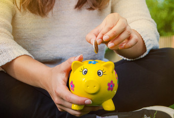 Teenager places coin into piggy bank to save for the future