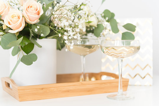 Blush wedding bouquet with roses, baby's breath and eucaluptus in wooden tray with wineglasses, present bag