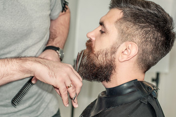 Men's hands cut a beard to a handsome young man. Barbershop