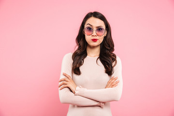 Photo of adult girl with brooding look and hands crossed looking on camera expressing resentment, isolated over pink background