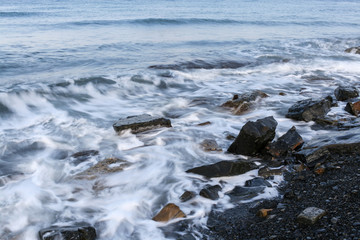 Sea waves are splashing on the stony shore. Long exposure.