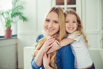 Smiling and happy mom and daughter are hugging each other at home on the couch. Mom and daughter  have fun. 