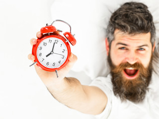 Man with yawning happy face lies on pillow, holds clock.