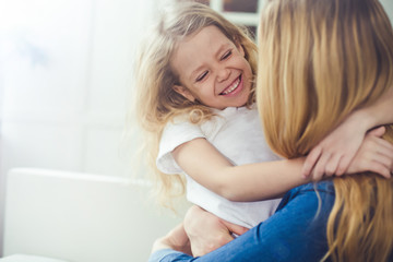 Smiling and happy mom and daughter are hugging each other at home on the couch. Mom and daughter  have fun. 