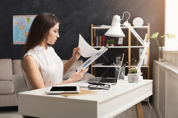 Serious woman at home working on laptop and reading documents