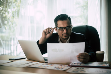 Businessman sitting at his workplace in front of laptop computer while doing some business paperwork.