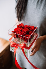 Obraz premium Woman holding transparent flower box filled with red roses with a red polka dotted bow on it