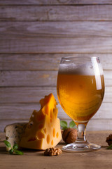 Beer and cheese. Glass of beer with cheese, walnuts and basil on wooden background. Ale and food concept