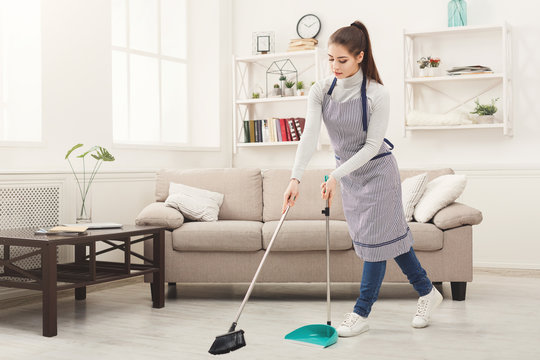 Young woman sweeping house with broom and scoop