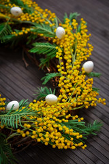 Wreath of mimosa with eggs on a brown background