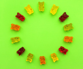 Gummy bears in different colors. Concept babies. Copy space. Rainbow halfcircle of colored sweet gummy bears on green background.