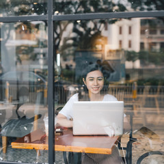 Asian woman working with laptop vintage color tone. Viewed through window of cafe.