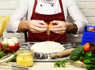 Cook in burgundy uniform works by table with vegetables