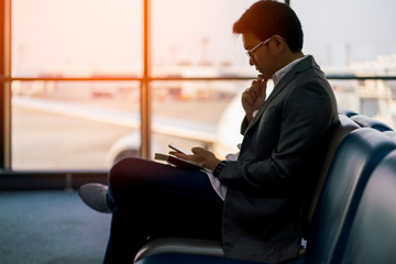 Young asian businessman sitting and using smartphone at waiting area in international airport