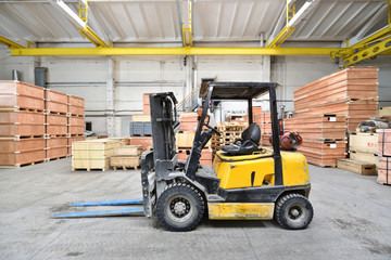 The forklift is old and scratched in a large and light warehouse. Yellow color - obrazy, fototapety, plakaty