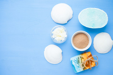 Spa and natural cosmetics concept. Set of skin and body care tools: shea oil, glass bottles, oil, soap, clay, shells фтв seaweed on the blue wooden background. Top view. Close up.