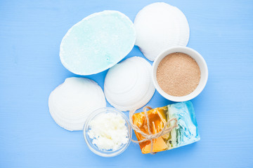 Spa and natural cosmetics concept. Set of skin and body care tools: shea oil, glass bottles, oil, soap, clay, shells фтв seaweed on the blue wooden background. Top view. Close up.