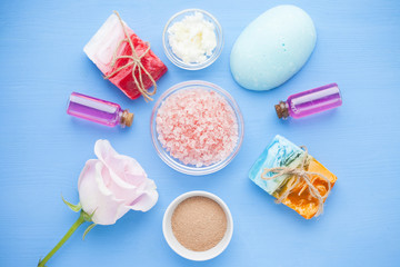 Spa and natural cosmetics concept. Set of sea salt, rose, natural clay ,shea oil, glass bottles and other spa treatment tools on the blue wooden background. Top view. Space for a text. Close up.