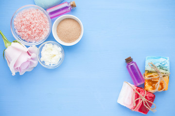Spa and natural cosmetics concept. Set of sea salt, rose, natural clay ,shea oil, glass bottles and other spa treatment tools on the blue wooden background. Top view. Space for a text. Close up.