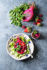 Vegan fruit salad with berries and mint served in pink dragon fruit with ingredients above on ceramic plate over blue texture background. Top view, space. Healthy eating