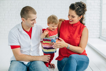 Young family of three sitting in white room. Little girl playing with russian doll. Mother father...