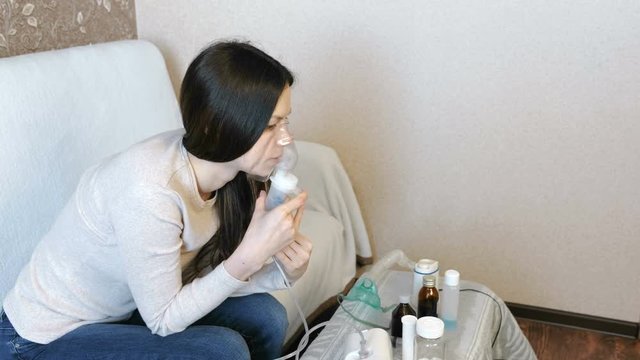 Use nebulizer and inhaler for the treatment. Young woman inhaling through inhaler mask. Side view.