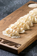 Asian dumplings Gyozas potstickers served with sesame on asian style wooden board over black texture background. Close up.