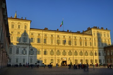 Turin, Italy, Piedmont, December 8 2017. The facade of the royal palace illuminated by the yellow light of the sun before sunset. Tourists visiting the city.