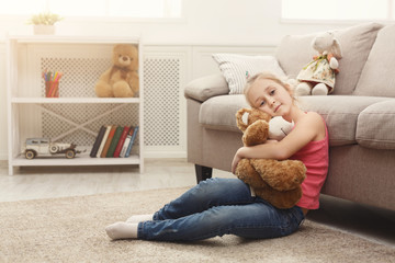Happy little female child hugging her teddy bear on the floor at home