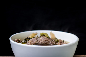 Pickled lettuce soup with spare rips in white bowl on wood and black background, Asian food, Dark tone