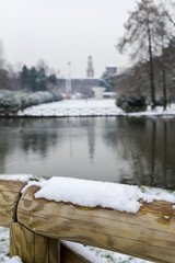 Selective focus of snow on wooden barrier with Sforza Castle, Italian: Castello Sforzesco, in Milan, northern Italy in background.