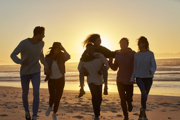 Silhouette Of Friends Having Fun Running Along Winter Beach