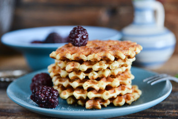 Dessert: round waffles with fresh berries blackberries and icing sugar on a wooden background.