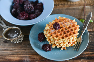 Dessert: round waffles with fresh berries blackberries and icing sugar on a wooden background.