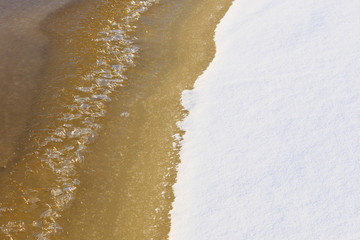 Edge of orange yellow water thawed from under a brilliant white snow.
