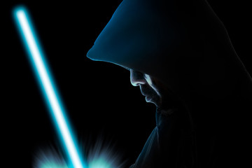 Man in hood / Hooded man in shadow with light sword on black background. - 195180277