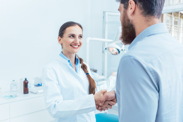 Portrait of a reliable and cheerful female dentist or dental surgeon shaking the hand of a patient...
