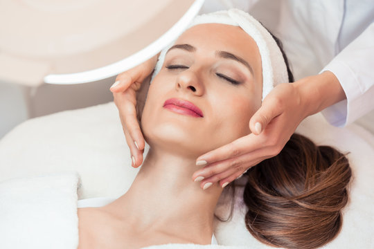 High-angle view of the face of a relaxed woman smiling under the benefits of anti-aging facial massage in a contemporary beauty center