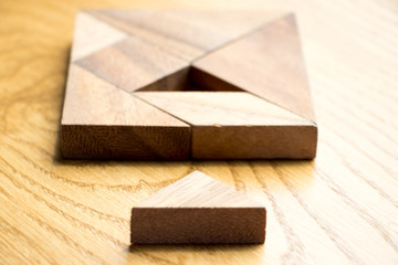 Tangram puzzle in square shape that wait for complete on wood background